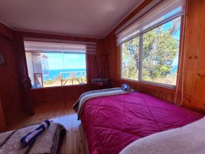 a bedroom with a purple bed and two windows at Refugio cabañas Bosquemar 2 in Queilén