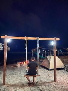 a man sitting on a bench in front of a tent at Rumahbatu beach cottage in Kuala Terengganu