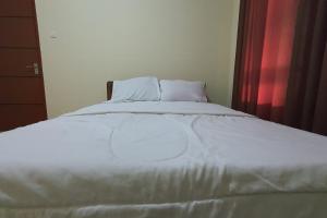 a bedroom with a white bed with a red curtain at Hotel O Karunia Kost & PenginapanNearSiring Marabahan (Ulek Barito) in Sungaisalai