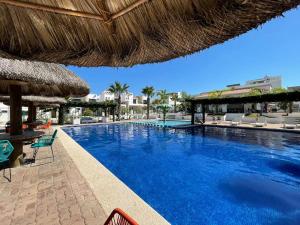 a large swimming pool with chairs and a straw umbrella at La casa del faro Azul Marino in Mazatlán
