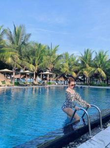 a woman sitting on a rail next to a swimming pool at Temple Da Nang Resort in Danang