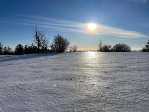 a snow covered field with the sun in the sky at Čertova bouda in Dolní Moravice