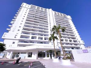 a large white building with a palm tree in front of it at Tropicalidays Paraiso Seafront in Playa Paraiso