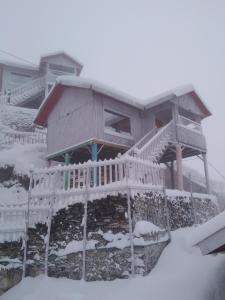 uma casa na neve com uma varanda em THE WONDERLAND COTTAGES & Cafe em Narkanda