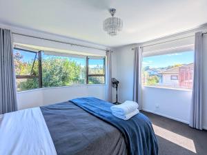 a bedroom with a bed and two large windows at Available Now! Family home near Redwood Forest in Rotorua