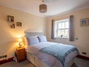 a bedroom with a bed with a blue comforter and a window at Bumble Cottage in Chipping Campden