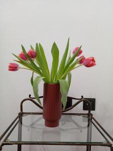 eine rote Vase mit rosa Blumen auf einem Glastisch in der Unterkunft VASO'S APPARTMENTS A in Mesolongi