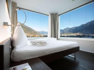 a bed in a room with a large window at Mercure Chur City West in Chur