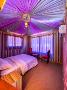 um quarto com um tecto roxo com uma cama e cadeiras em Alora Wadi Rum Luxury em Wadi Rum