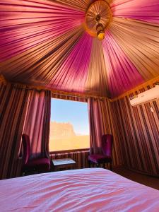 a bedroom with a bed and two chairs and a window at Alora Wadi Rum Luxury in Wadi Rum