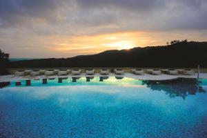 a swimming pool with chairs and the sunset in the background at Mercure Petriolo Siena Terme Spa Hotel in Terme di Petriolo