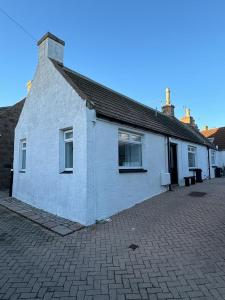 a white house with a brick driveway in front of it at The Harbour Cottage in Peterhead