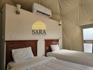 two beds in a tent with a sign on the wall at SARA LUXURY RUM CAMp in Wadi Rum