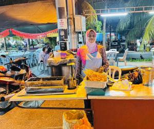 Eine Frau steht vor einem Tisch mit Essen. in der Unterkunft ShopLot Hostel Pangkor in Kampong Pasir Bogak