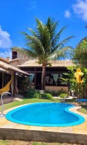 a swimming pool in front of a house with a palm tree at Pousada Aconchego de Genipabu in Jenipabu