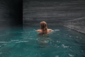 Kobieta siedzi w basenie z wodą. w obiekcie 7132 Hotel w mieście Vals