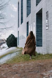 a woman in a cloak walking past a building at 7132 Hotel in Vals