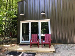two red chairs sitting on a porch next to a building at Hockey Themed Room with Wooded Trails in Benzonia