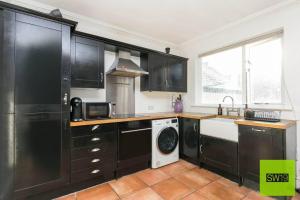 a kitchen with black cabinets and a washer and dryer at Modern 2 Bedroom with Free Parking & near Tube in London