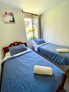 a room with two beds with blue sheets and a window at Apartamentos Alma Surire in Arica
