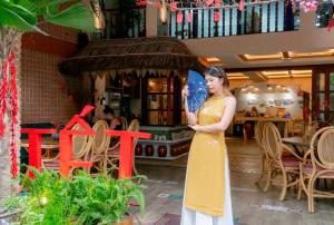 une femme en robe jaune tenant un ventilateur bleu dans l'établissement Seahorse Signature Danang Hotel by Haviland, à Đà Nẵng