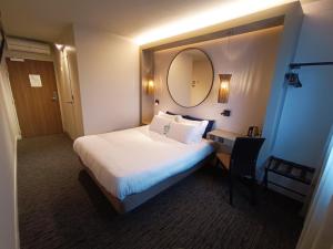 Pokój hotelowy z łóżkiem i lustrem w obiekcie Hôtel Kyriad Brive Ouest w mieście Brive-la-Gaillarde