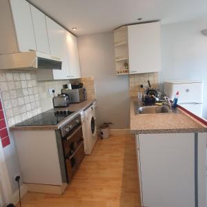 a kitchen with white cabinets and a sink and a dishwasher at Flat with excellent transport links to central London. in Elmers End