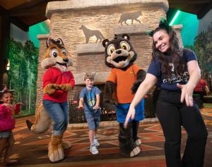 a woman and two mascots and a child walking in front of a fireplace at Great Wolf Lodge Chicago/Gurnee in Gurnee