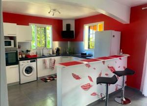 een keuken met rode muren en een aanrecht met krukken bij Studio avec jardin et wifi a Le Moule a 5 km de la plage in Le Moule