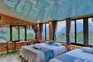 two beds in a room with large windows at Hang Mua Bamboo Homestay Ninh Binh in Ninh Binh