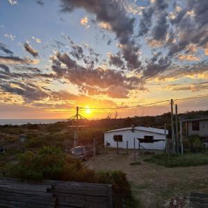 una puesta de sol sobre un campo con un edificio y un coche en La casa de Juan en Cuchilla Alta