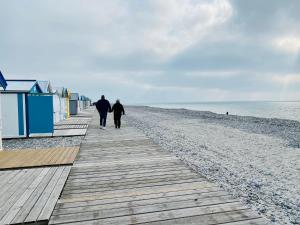 two people walking down a boardwalk on a beach at Maison de pêcheur rénovée à 3 mn de la mer. in Cayeux-sur-Mer