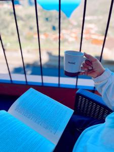 a person holding a cup of coffee and a book at Gardens Guest House in São Vicente