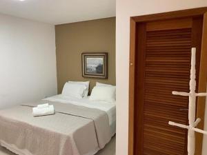 um quarto com uma cama branca e uma porta de madeira em Espaço Hale Kai em Guarapari