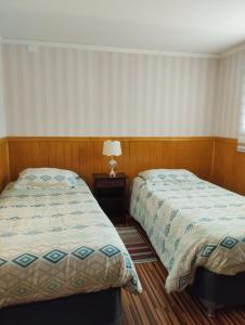 a bedroom with two beds and a table with a lamp at Cabañas Marina del Sur 1 in Puerto Natales