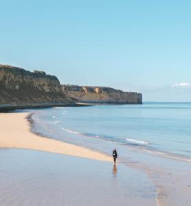 a man walking on a beach near the water at Maison rénovée cour fermée et terrasse 800 m plage Omaha beach avec table de ping pong proche Port en Bessin in Vierville-sur-Mer