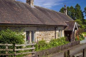 una vieja casa de piedra con una valla delante de ella en Garden Cottage Haughton Castle 2 en Hexham