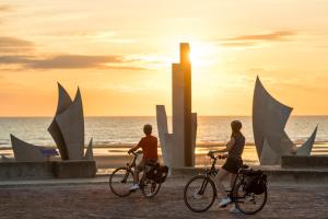 Dos personas montando en bicicleta en la playa al atardecer en Maison lumineuse spacieuse deux vérandas grand jardin pres Port en Bessin et Bayeux, proche plages du débarquement, en Commes