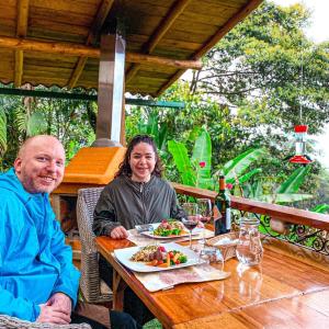Ein Mann und eine Frau sitzen an einem Tisch mit einem Teller Essen. in der Unterkunft Casa de Vista Alta in Mindo