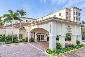 Homewood Suites by Hilton Palm Beach Gardens في بالم بيتش غاردن: مبنى الفندق مع بوابة والنخيل