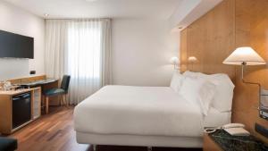 マドリードにあるNH パセオ デ ラ ハバナのベッド、デスク、電話が備わるホテルルームです。