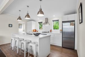 a kitchen with white cabinets and a large island with bar stools at Relax on Dillon - Waihi Beach Holiday Home in Waihi Beach