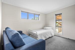 a living room with a blue couch and a bed at Relax on Dillon - Waihi Beach Holiday Home in Waihi Beach