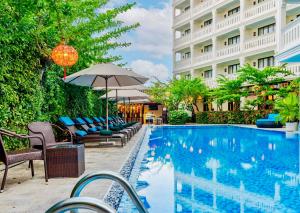 a swimming pool with chairs and an umbrella next to a building at Wyndham Garden Hoi An Cua Dai Beach in Hoi An