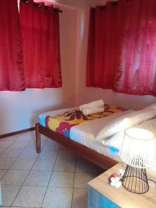 uma cama num quarto com cortinas vermelhas e um candeeiro em Vaiana Home 2 - bord de lagon em Taputapuapea