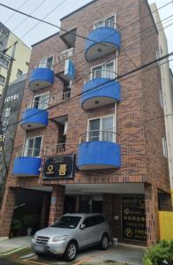un coche aparcado frente a un edificio con balcones azules en Oreum Motel en Jeju