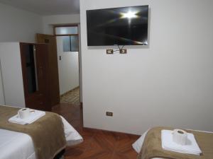 Habitación con 2 camas y TV de pantalla plana en la pared. en Hospedaje EL RINCONCITO II, en Jauja