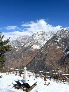 a snow covered mountain with chairs and an umbrella at Faraway Cottages, Auli in Joshīmath
