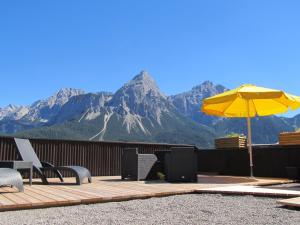 a deck with chairs and an umbrella and mountains at Alpenstern Pension Suites in Lermoos