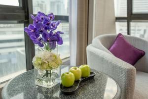 a glass vase with purple flowers and apples on a table at Boulevard Hotel Bangkok Sukhumvit in Bangkok